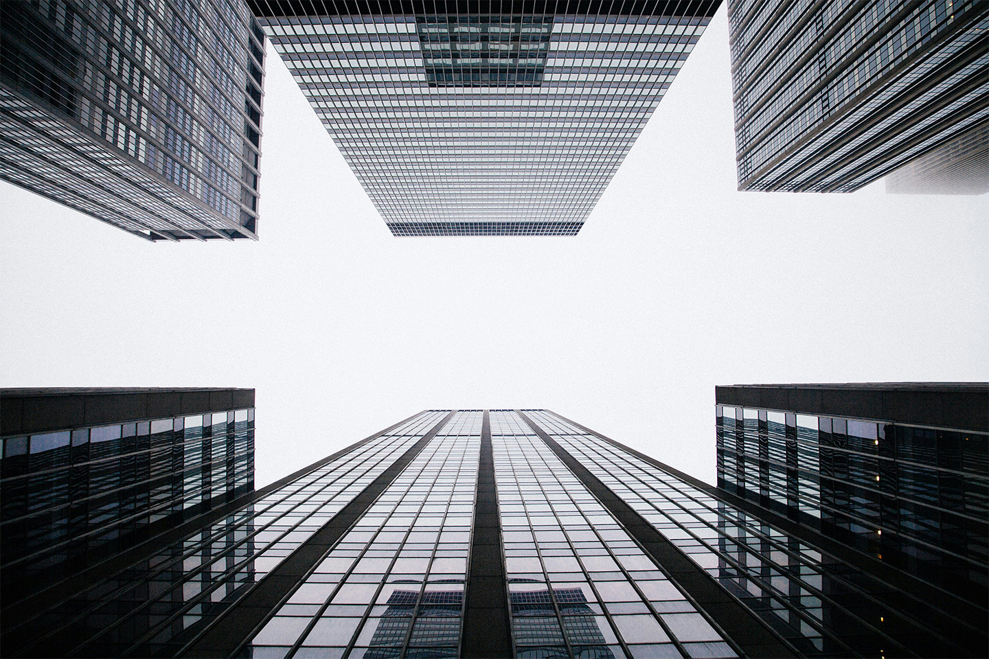 Black and white photo of high rise buildings pictured from the middle of a street looking straight up