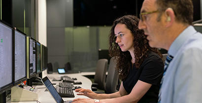 A woman and a man looking at multiple computer screens in discussion