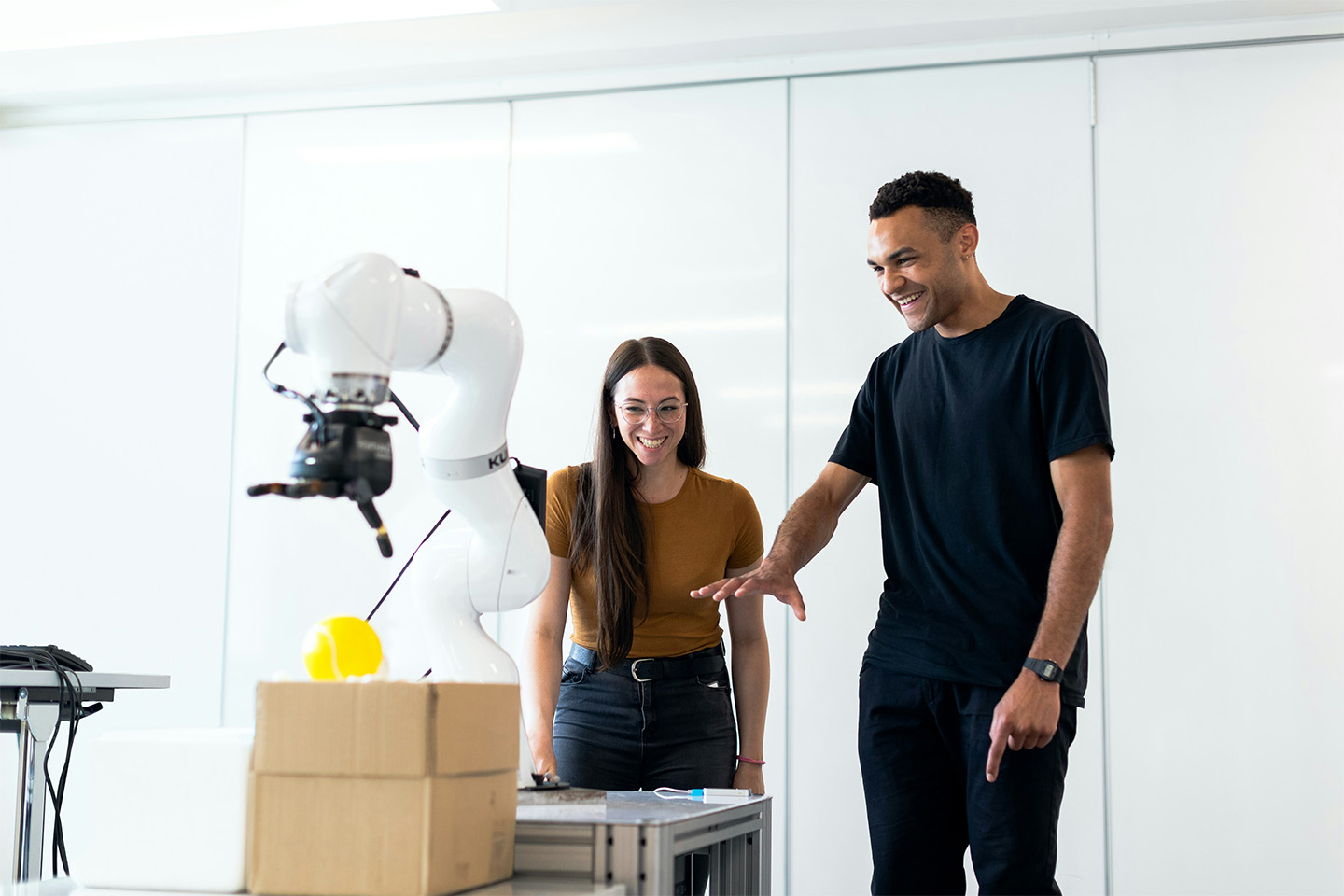 A man and a woman standing behind a large robotic arm 