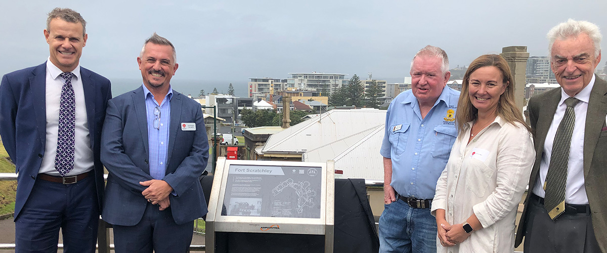 Group of engineers and council representatives stand around the Fort Scratchley heritage marker plaque
