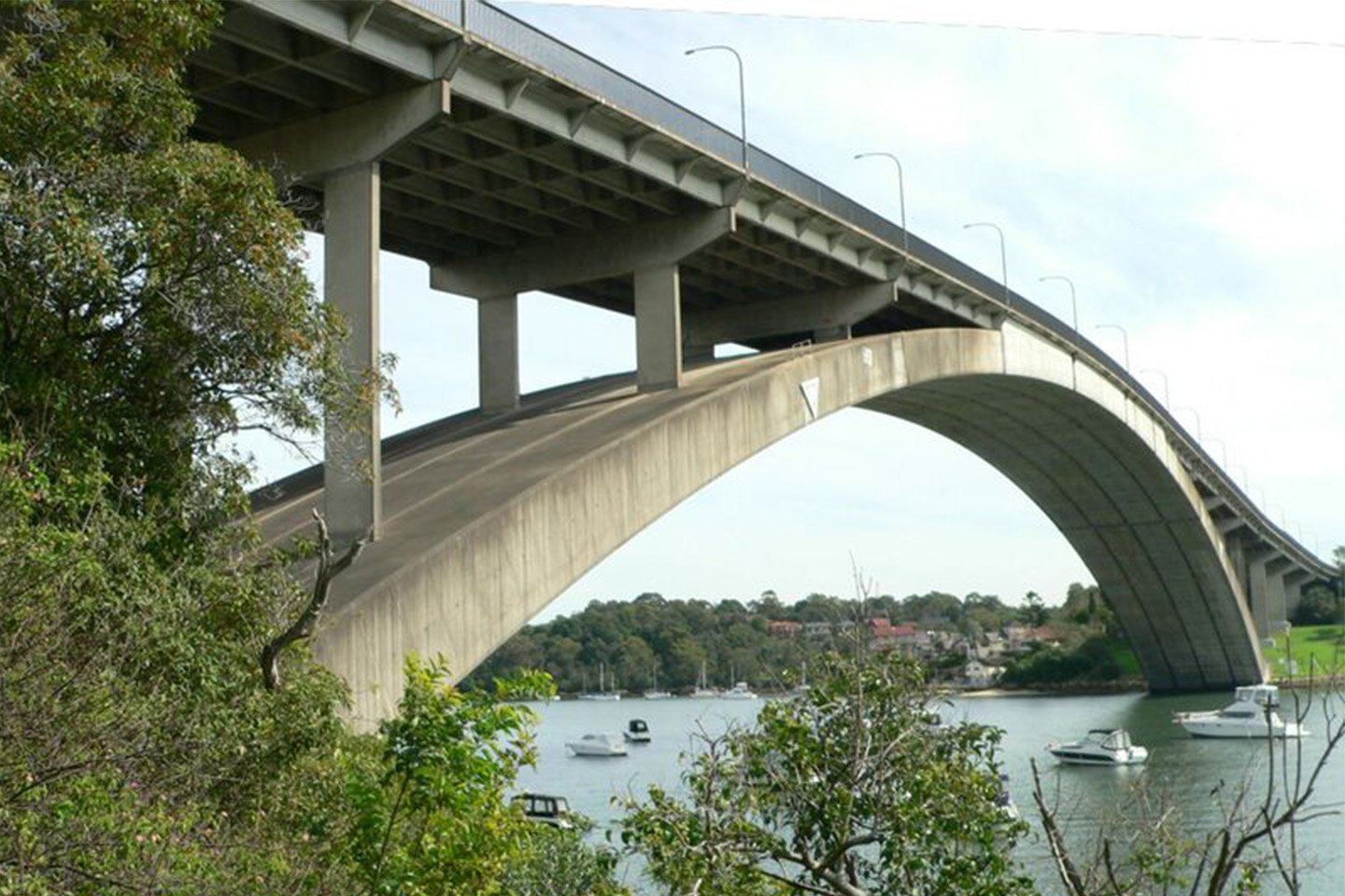 Long concrete bridge with a large archway underneath and plants in the foreground of the photo