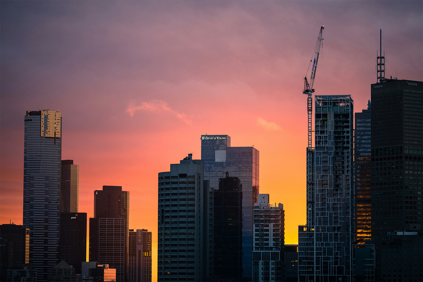Melbourne skyline at night with high rise buildings of different sizes in front of an orange and pink sky