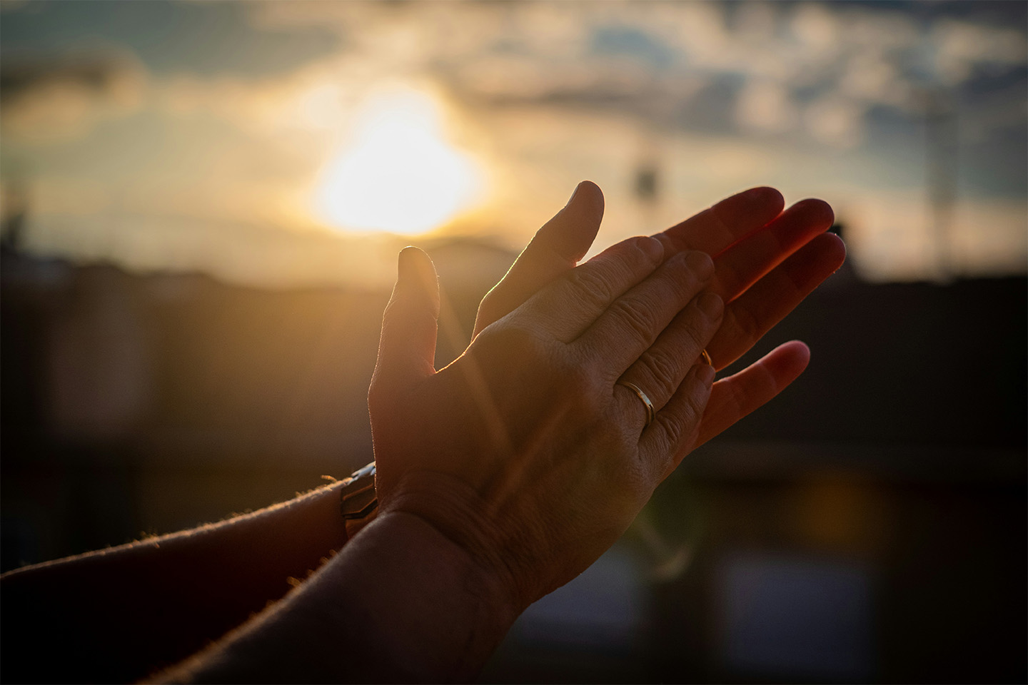 Pair of hands coming together in a clapping motion in front of a sunset