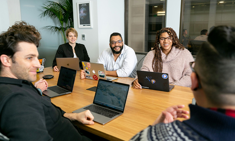 Four people sitting at desk on laptops.