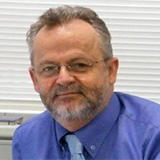 Image of an older man in a blue shirt smiling at the camera