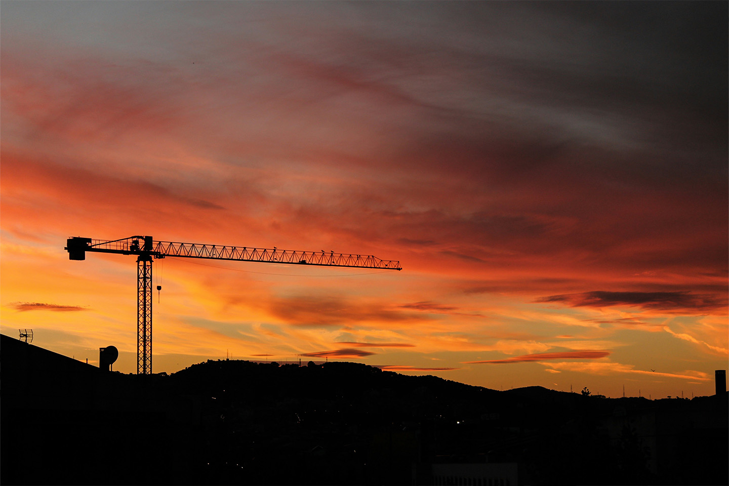 sun setting in orange and red tones with a crane in shadow in the left hand corner of the image