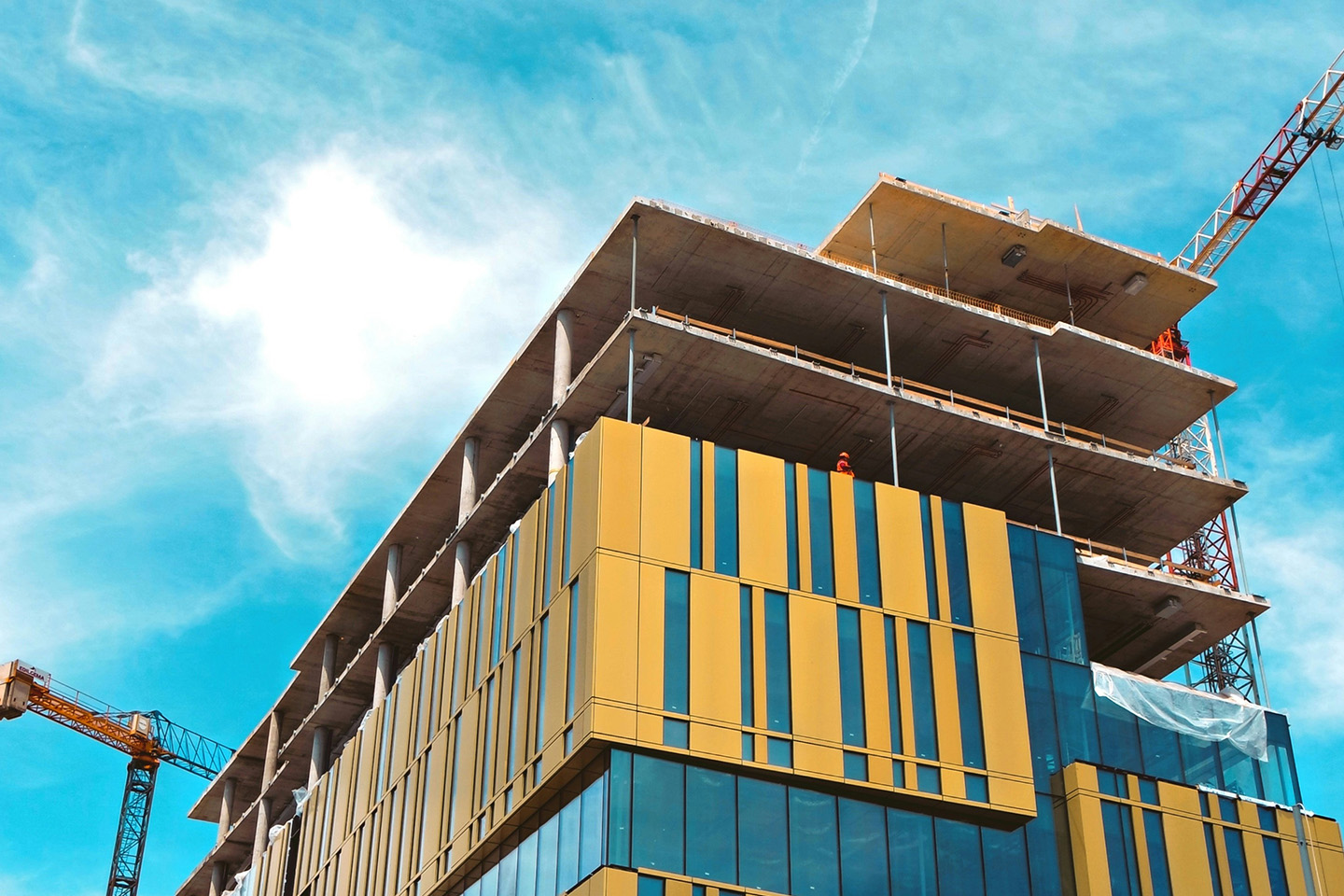 two cranes working on a high rise building with blue sky behind