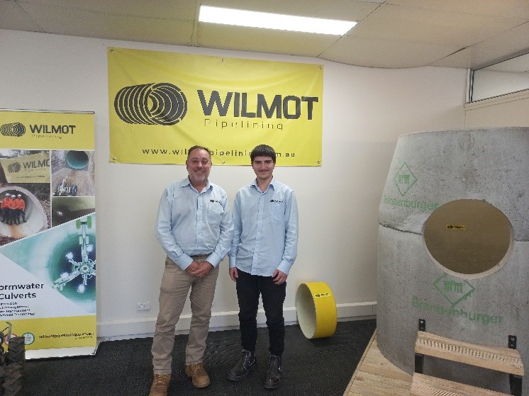 Newcastle student stands with a man from the pipeline company he did work experience with in front of the company's yellow logo