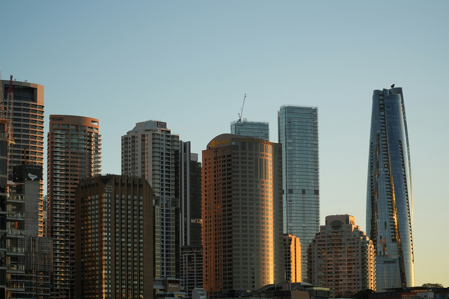 Multiple high rise buildings in front of blue sky as the sun is rising behind them