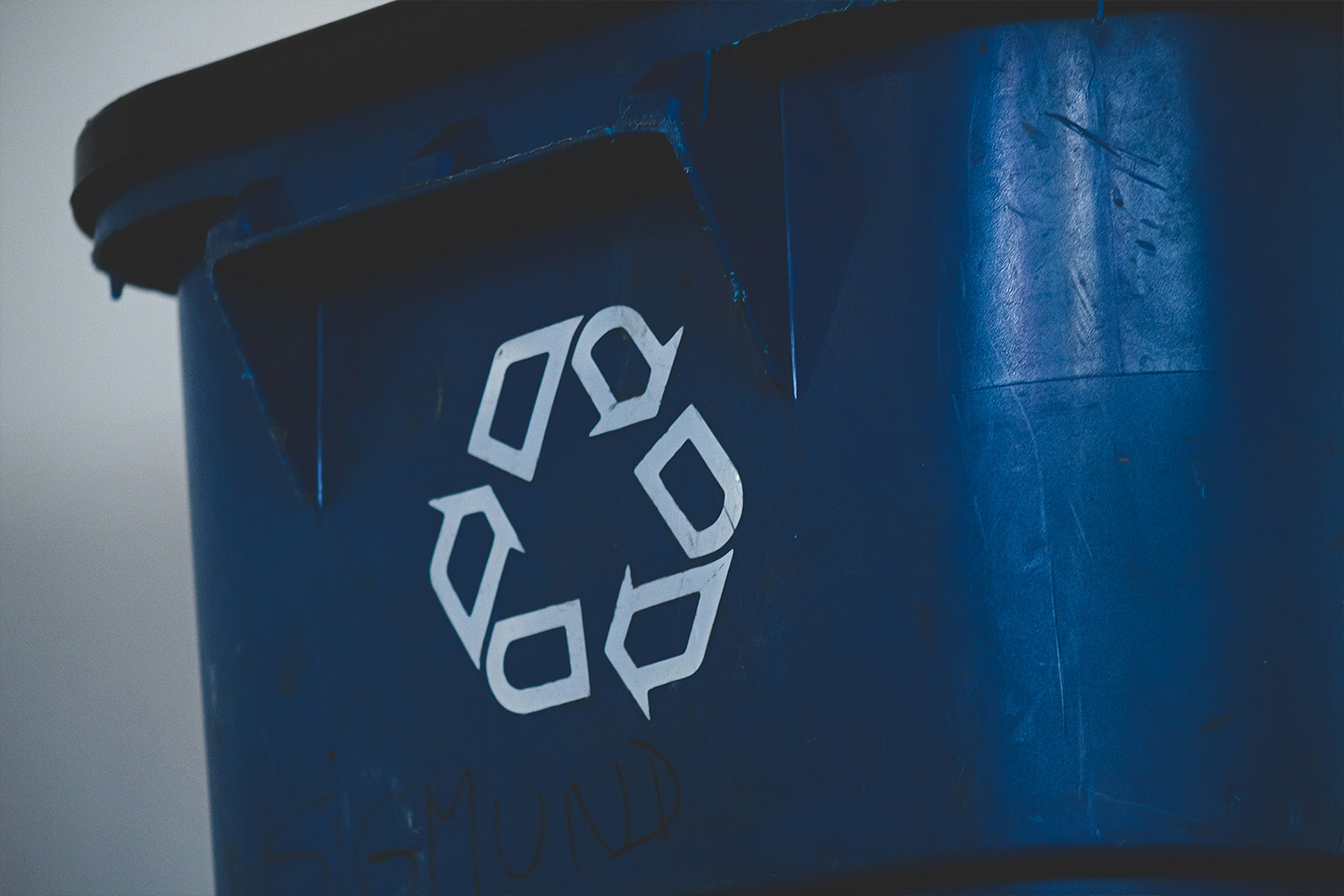 Blue bin with the recycling symbol on it, three arrows that form a triangle