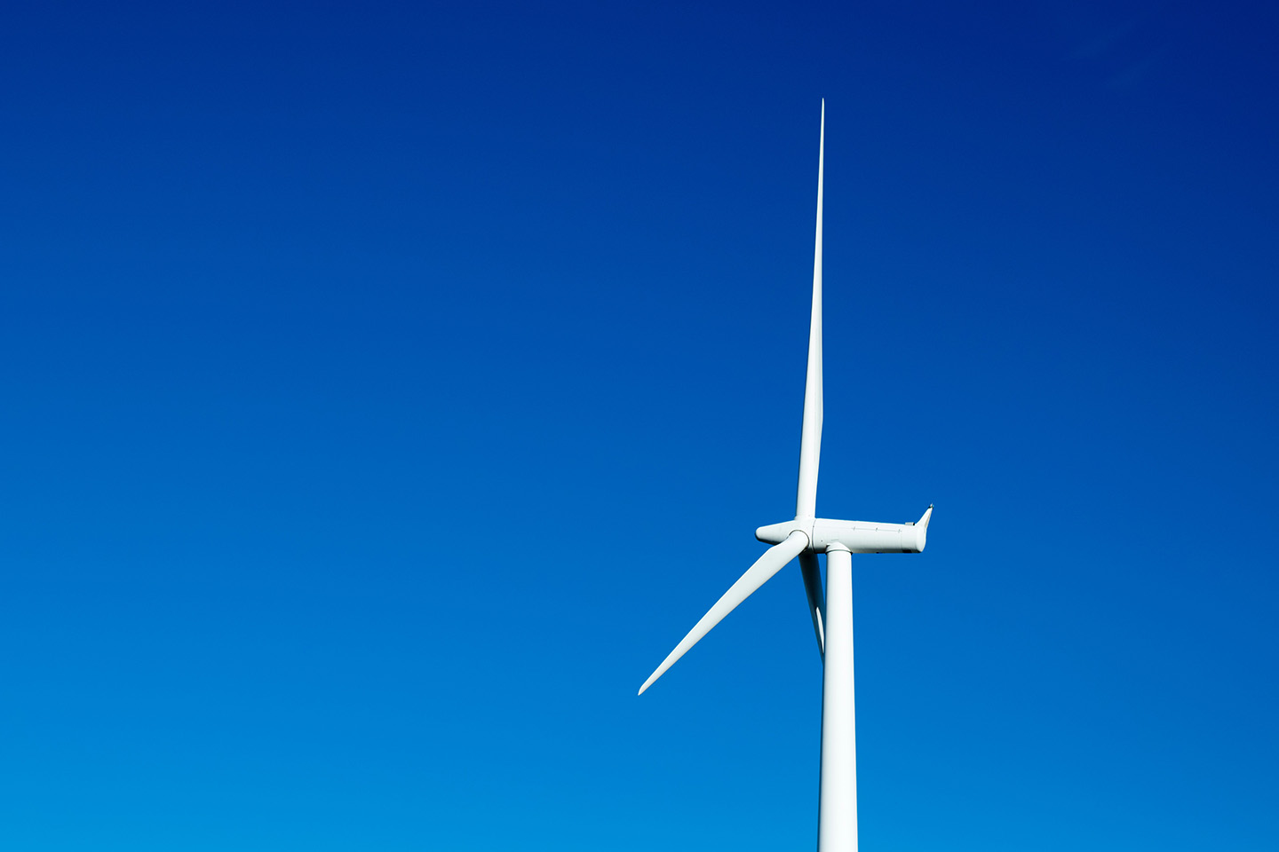 One white wind turbine side on with blue sky in the background