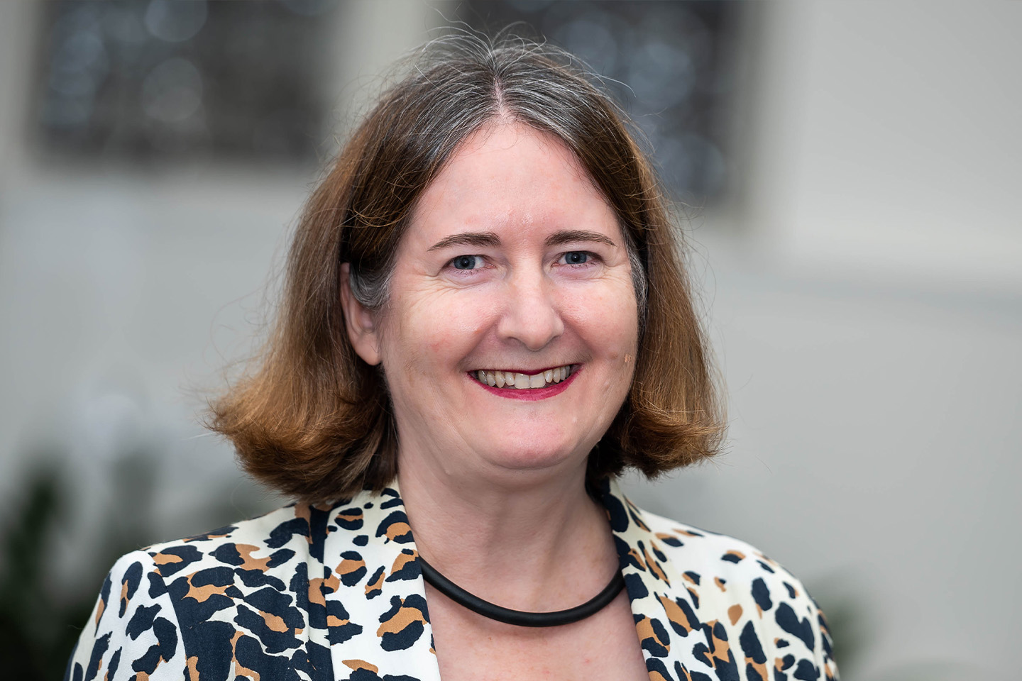 Sally smiling for a profile shot wearing a white, black and orange patterned blazer