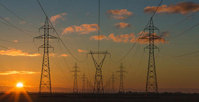 Three large power poles pictured at sunset with an orange sky behind
