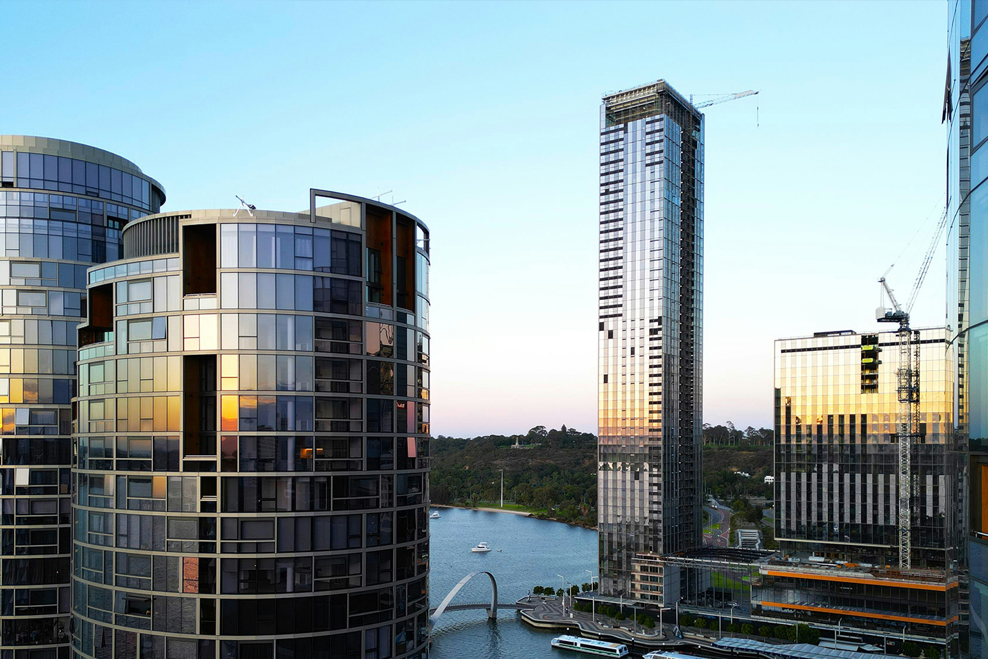 High rise buildings down by a river, two with cranes on top being built